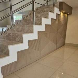 Painel sob escada restaurado com laqueamento decorativo, destacando seu design renovado. A reforma incluiu iluminação embutida, otimizando o espaço com estilo e funcionalidade.
