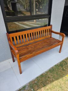 Foto de um banco restaurado com acabamento verniz marítimo em baixo de uma janela preta